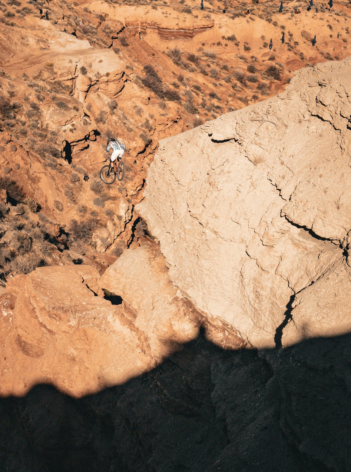 Person mountain biking on a rocky cliff edge with desert landscape below