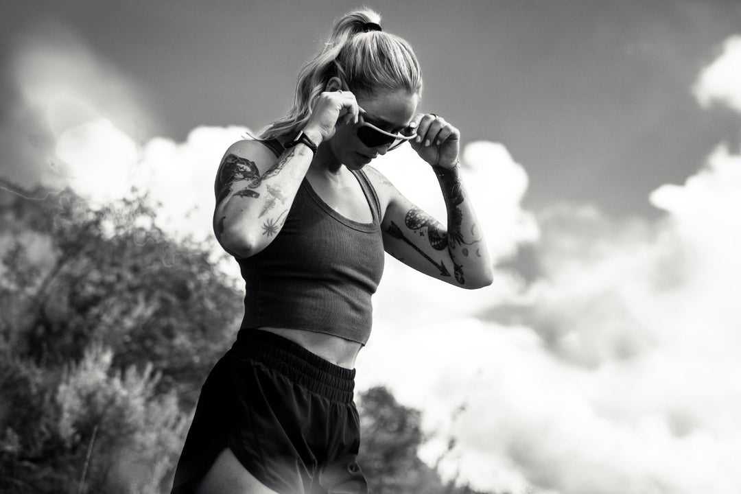 Person in athletic wear adjusting sunglasses outdoors with a natural background