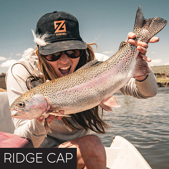 Person holding a large fish on a boat with a Zirkel Ridge Cap featuring logo.