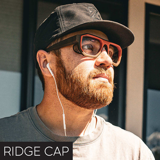 Man wearing a black cap and red sunglasses with earphones, with 'RIDGE CAP' text at the bottom.